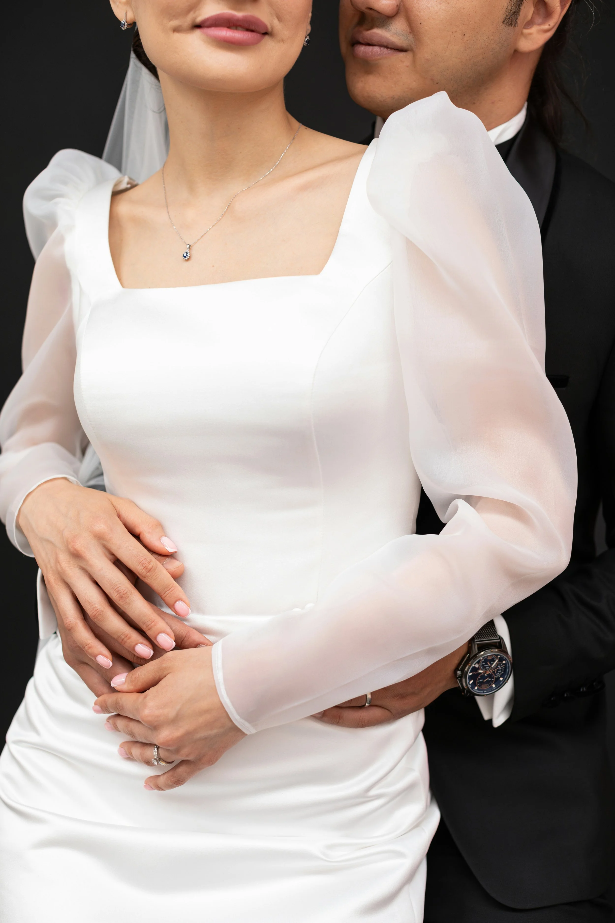A couple in wedding attire with the woman's white dress and the man's black tuxedo, embracing close.