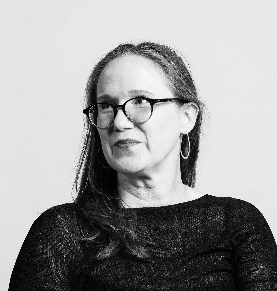 Black and white portrait of a woman with glasses and hoop earrings, looking to her left.
