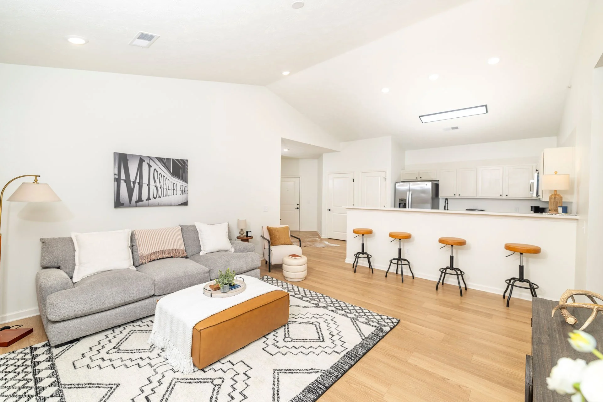 Living room with gray sofa, black and white geometric rug, white wall art, and bar stools at kitchen counter.