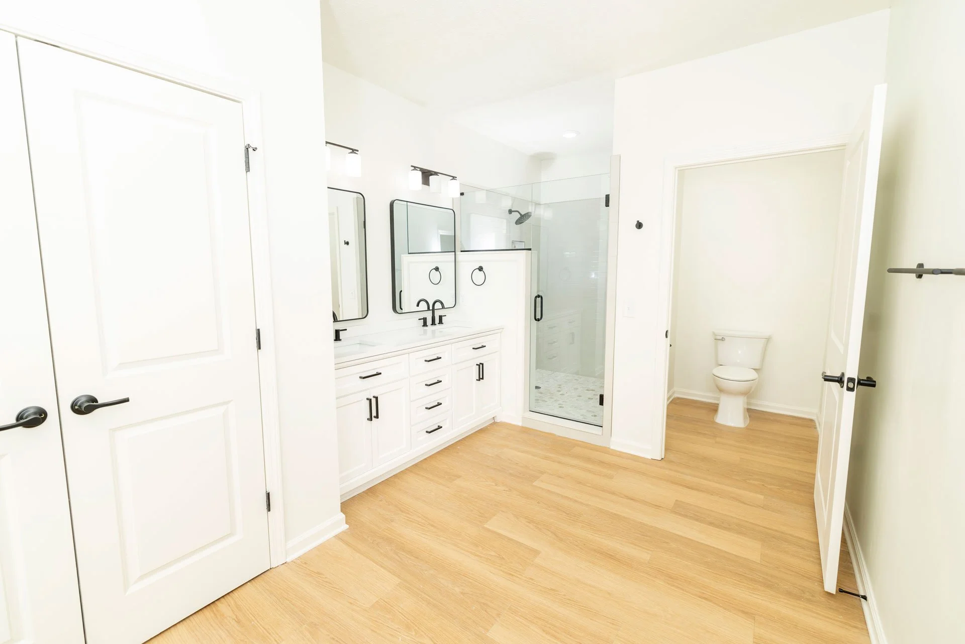 Modern bathroom with white vanity, black fixtures, dual mirrors, glass shower enclosure, and separate toilet area.