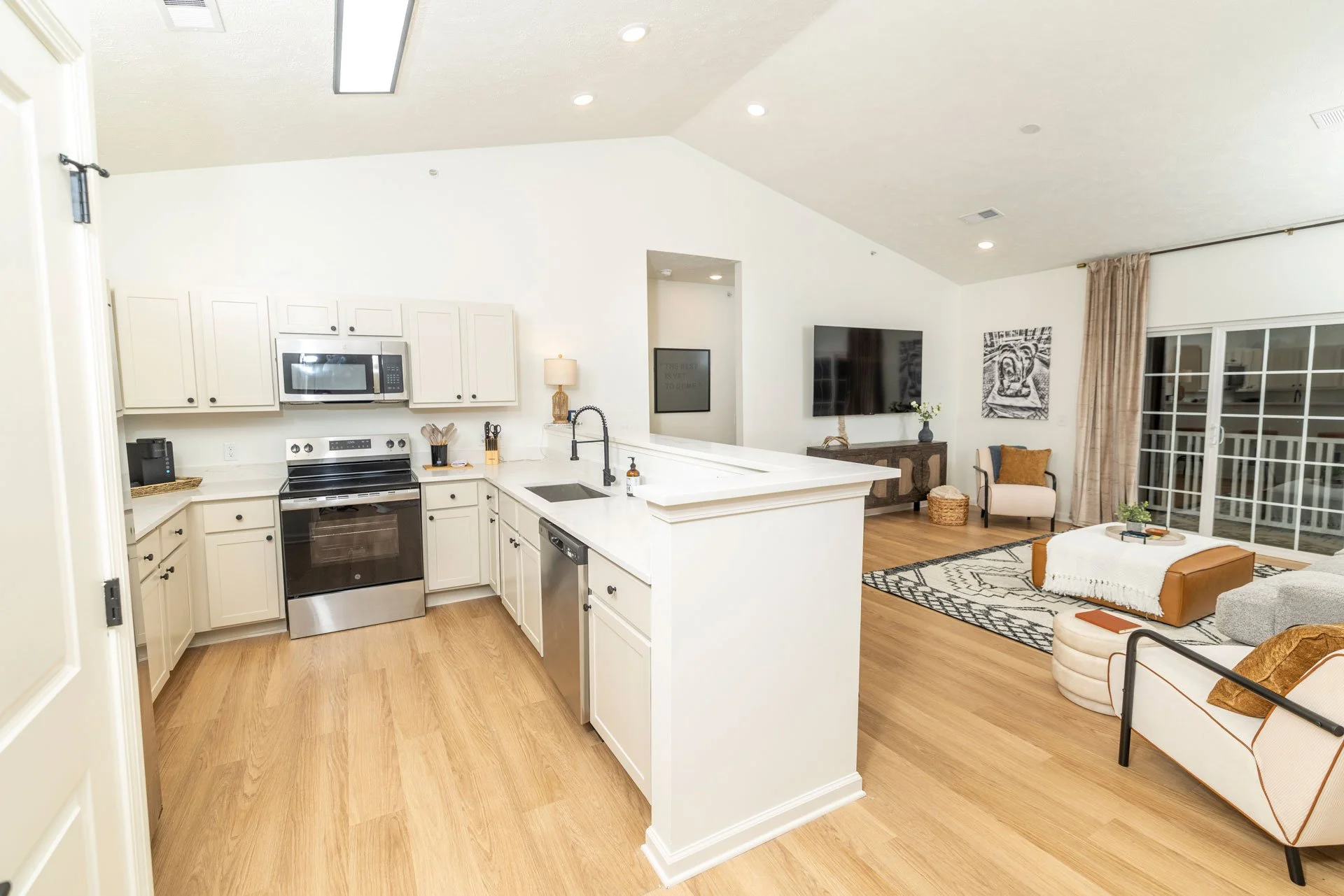 Open-concept living room and kitchen with white cabinets, stainless steel appliances, wooden flooring, and modern furniture and decor.