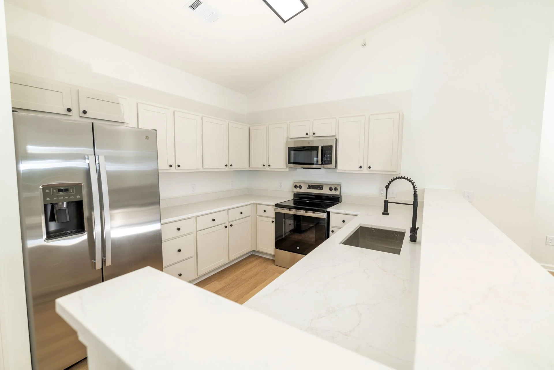 Modern kitchen with white cabinets, stainless steel refrigerator, black stove, microwave, and black faucet