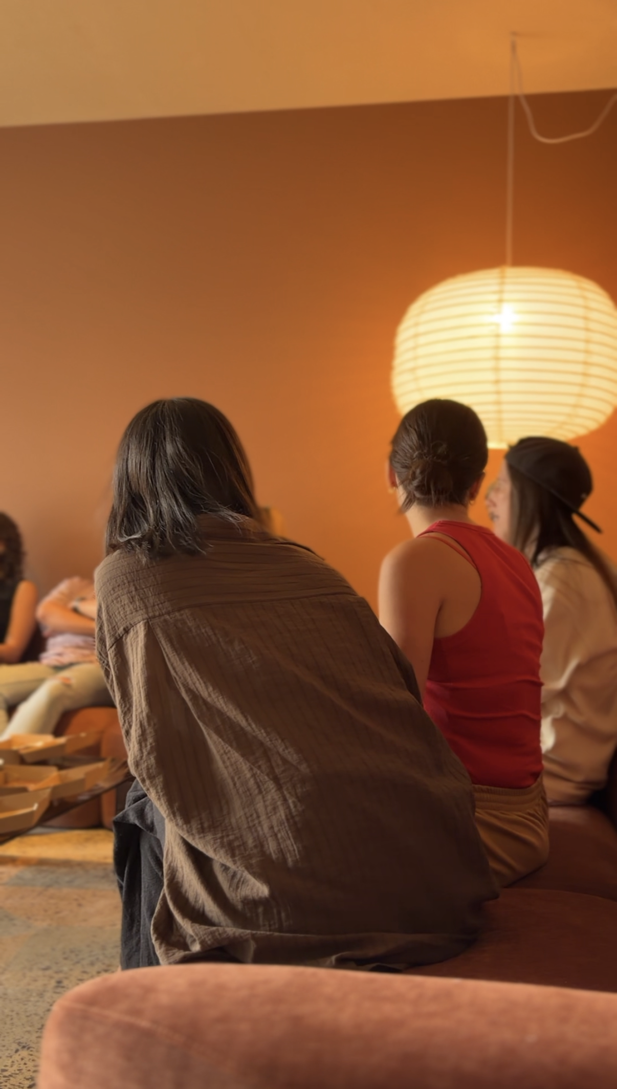 People sitting in a cozy, warmly lit room with orange walls and a paper lantern hanging from the ceiling.