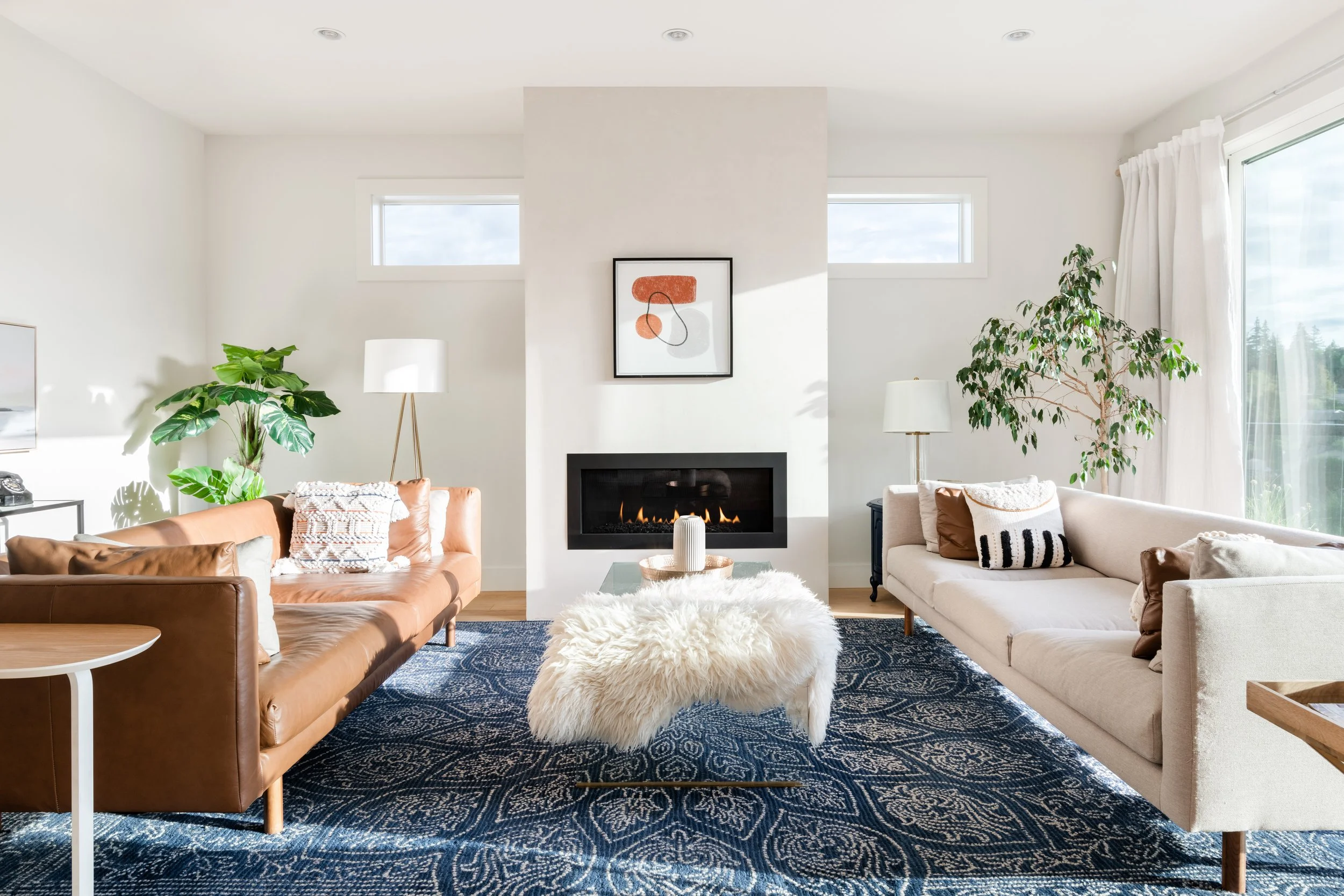 Modern living room with two sofas flanking the fireplace. Symmetrical layout in a modern style with Blue wool area rug, sheep skin accessory and abstract art. Interior Design for homes and business Victoria BC