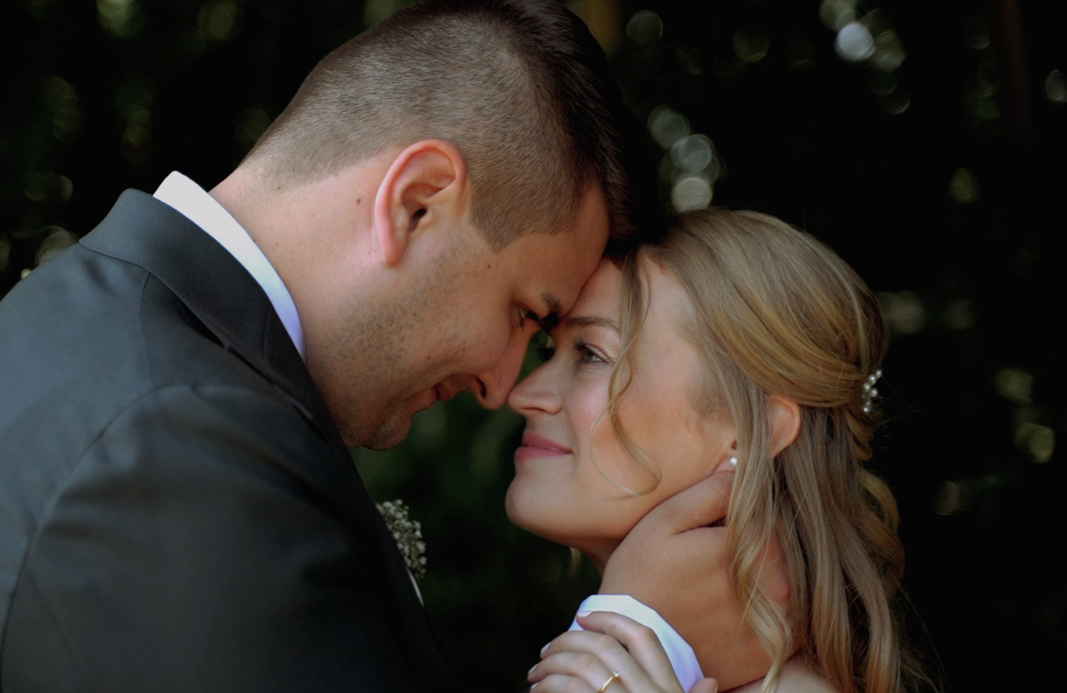 Ein Hochzeitspaar in einer intimen Umarmung, ihr Gesicht berührt sich, im Hintergrund unscharfe Natur.