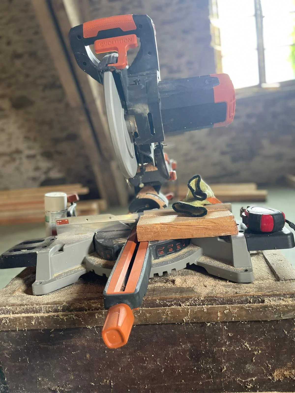 A miter saw on a workbench in a woodworking shop, with a piece of wood and a measuring tape nearby.