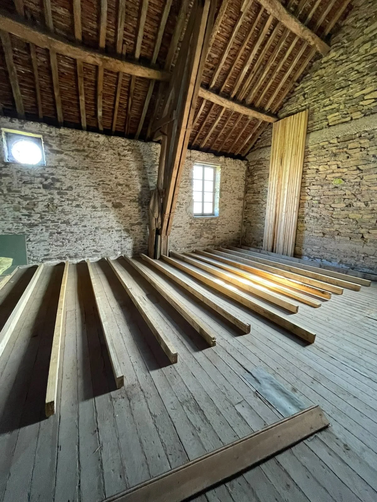 Interior of an unfinished room with exposed brick walls, wooden beams, and a partially constructed floor with wooden joists.