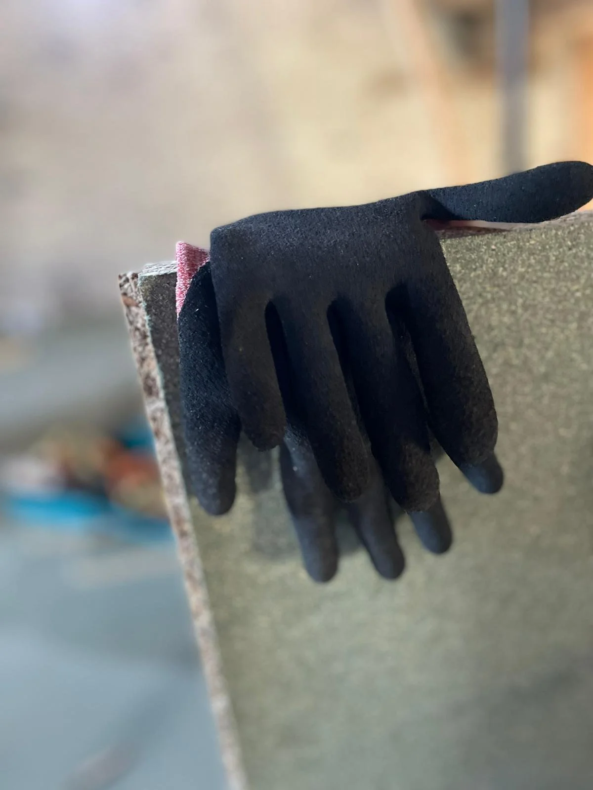 Black work gloves hanging on a dusty workbench in a workshop.