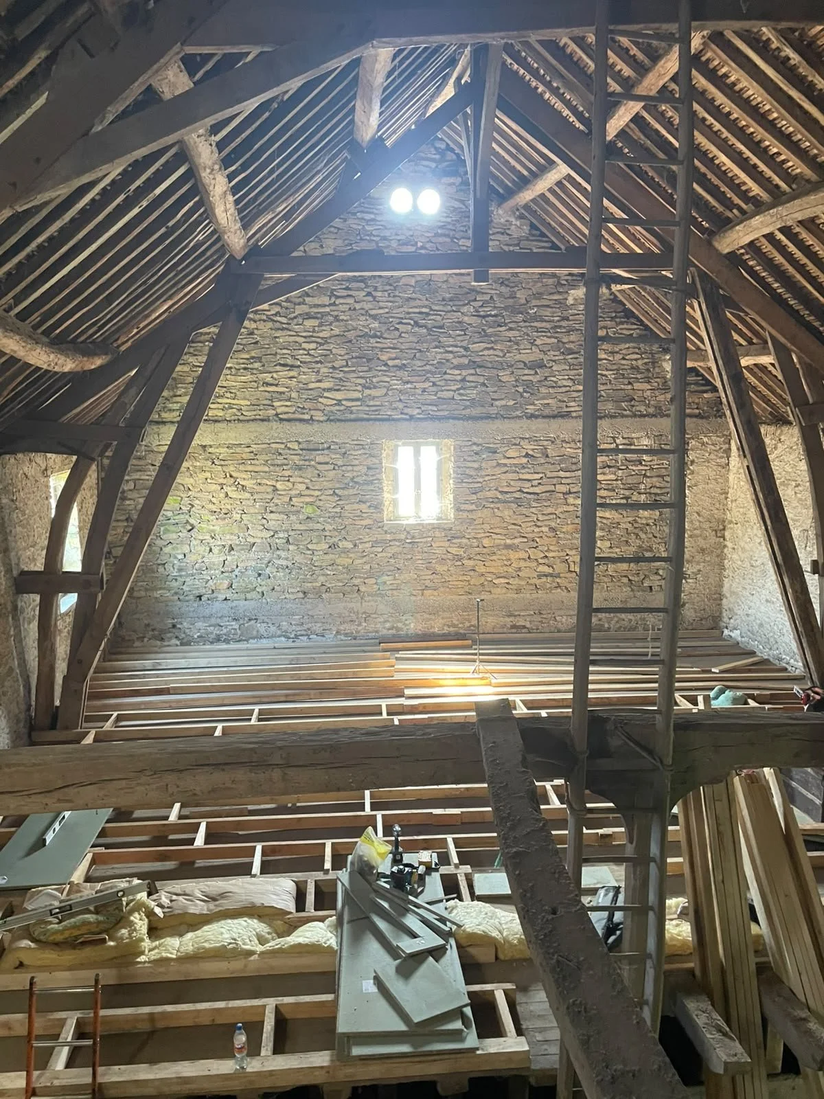 Interior of an attic under construction with wooden framing, brick walls, and a small window.