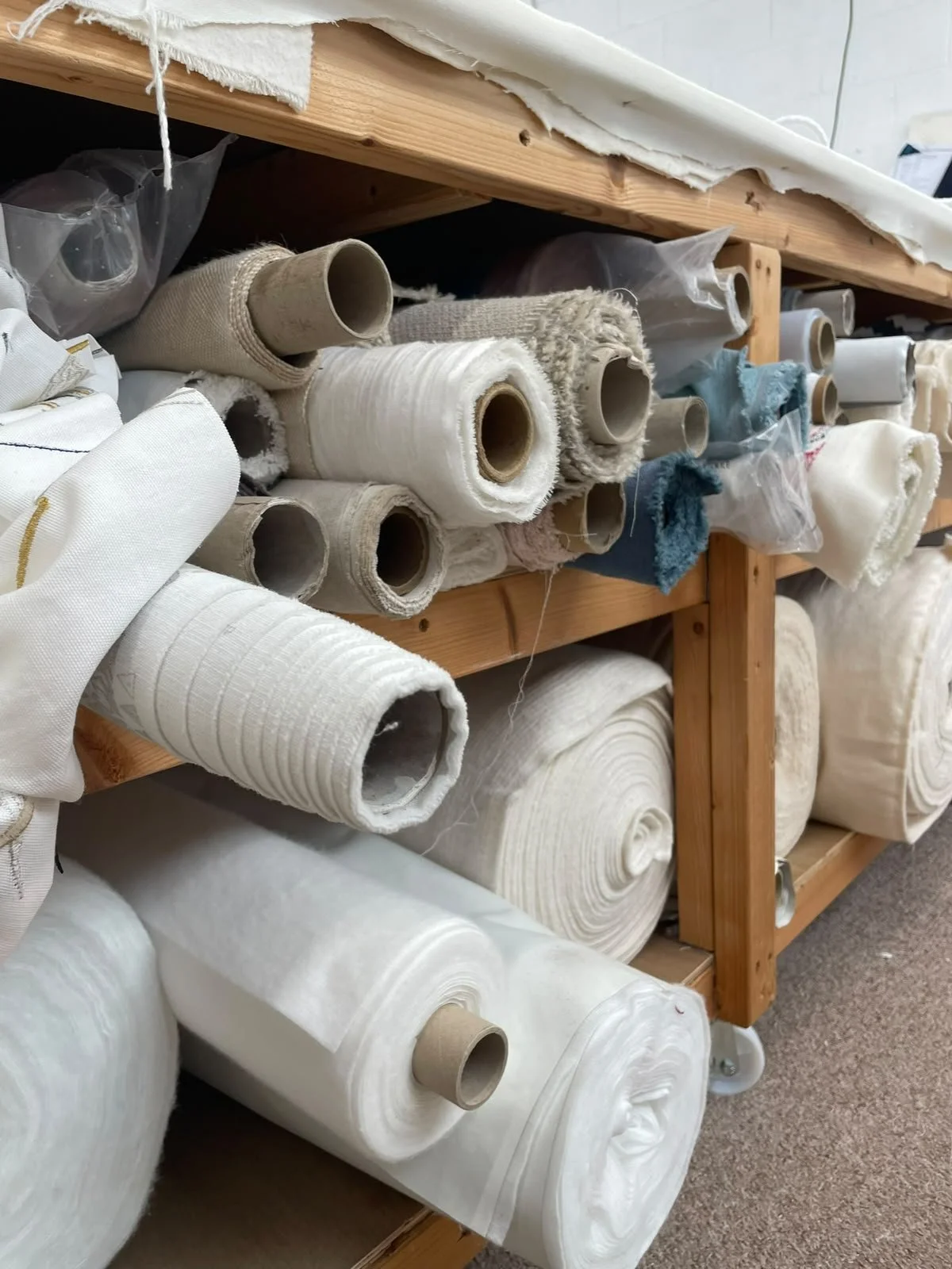 Shelves with rolls of fabric and textiles, including white and beige fabrics, in a storage or warehouse setting.
