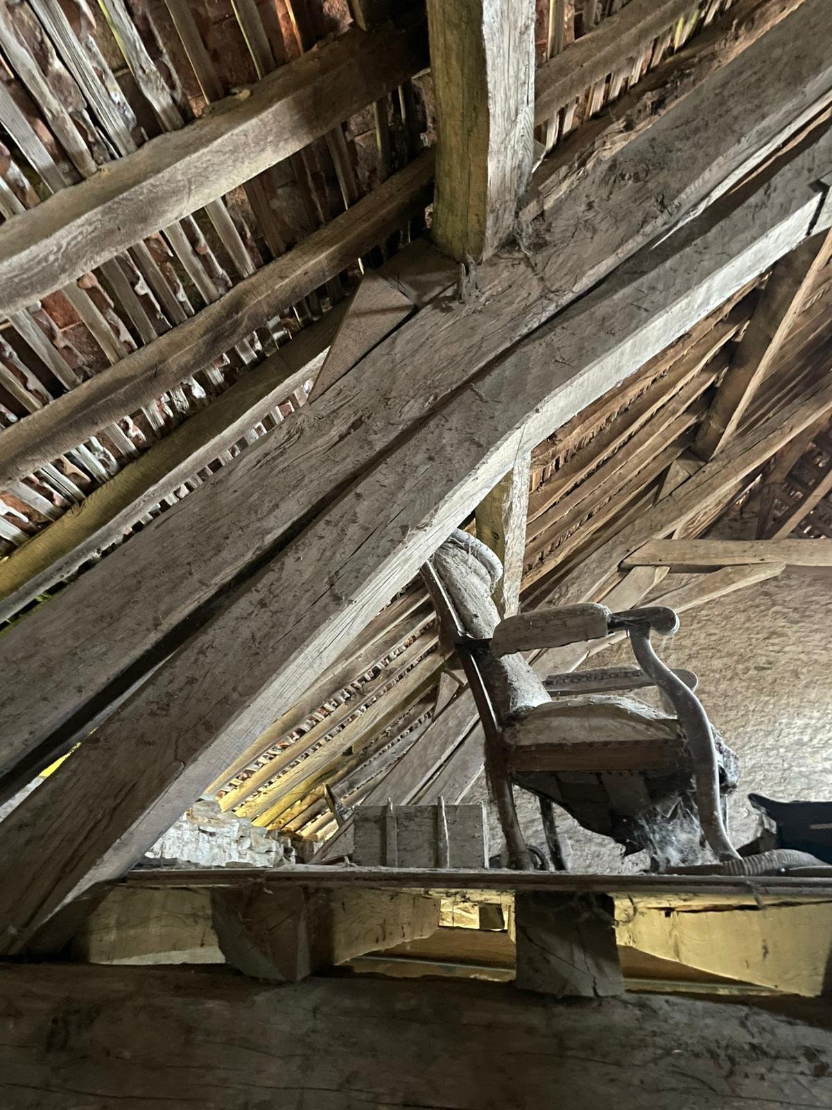 An old wooden chair in an attic with a rustic, weathered wooden ceiling and beams.