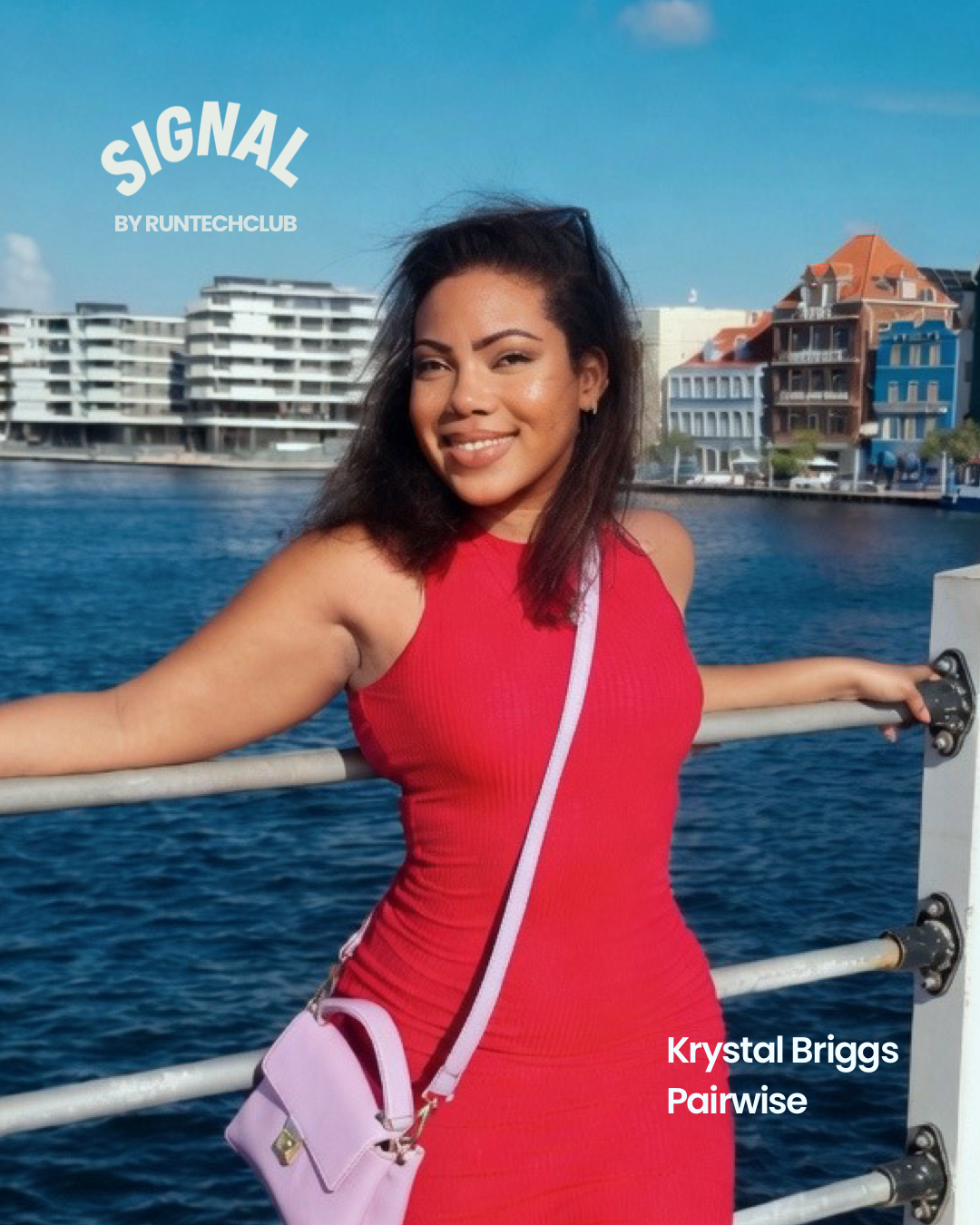 A woman in a red dress leaning on a waterfront railing, smiling, with water and modern buildings in the background.