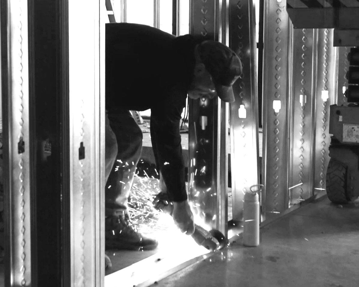 A person welding metal inside a building under construction, with sparks flying from the welding process.