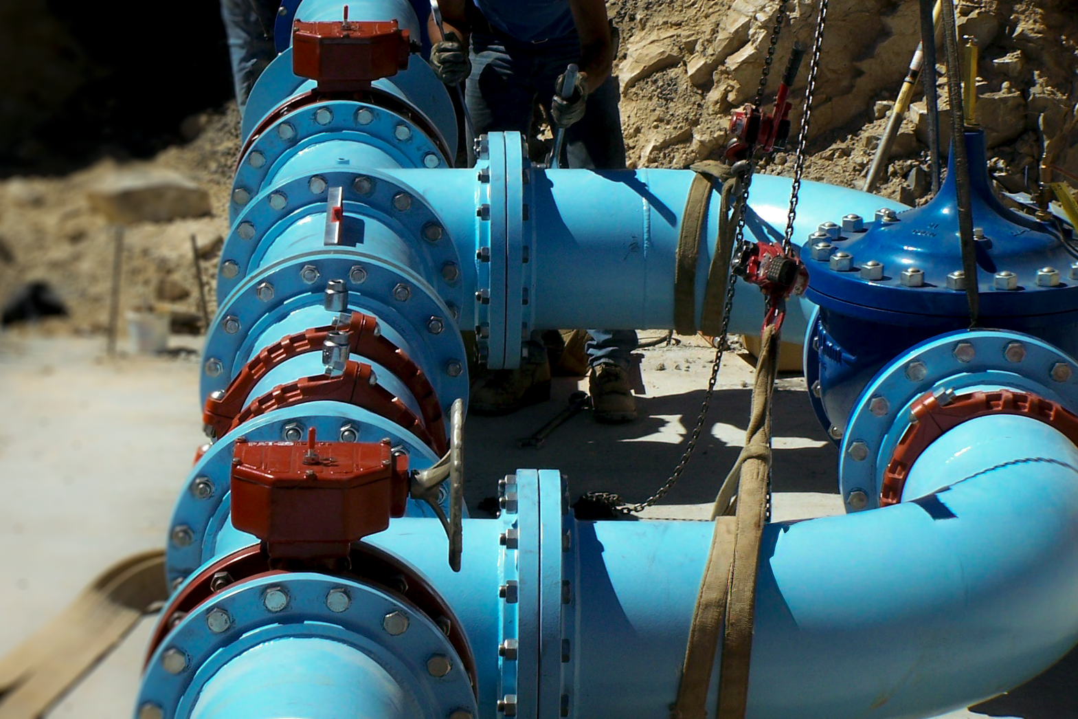 Large blue industrial pipes connected with bolt flanges at a construction site with workers present.