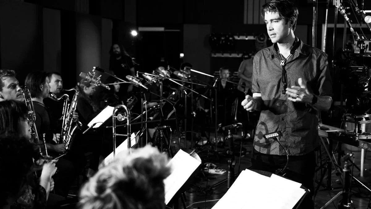 Black and white. Orchestra being addressed by man