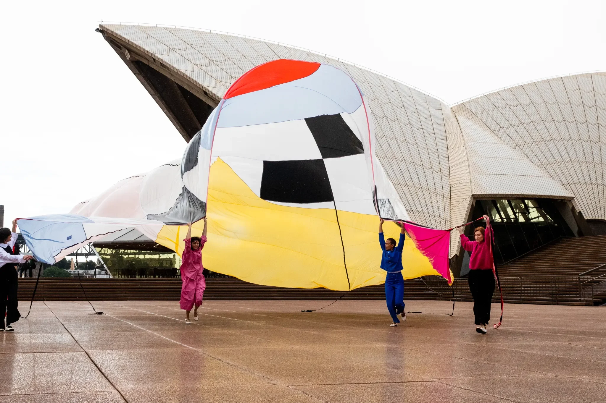 Performers holding large fabric in the wind in front of the Opera House