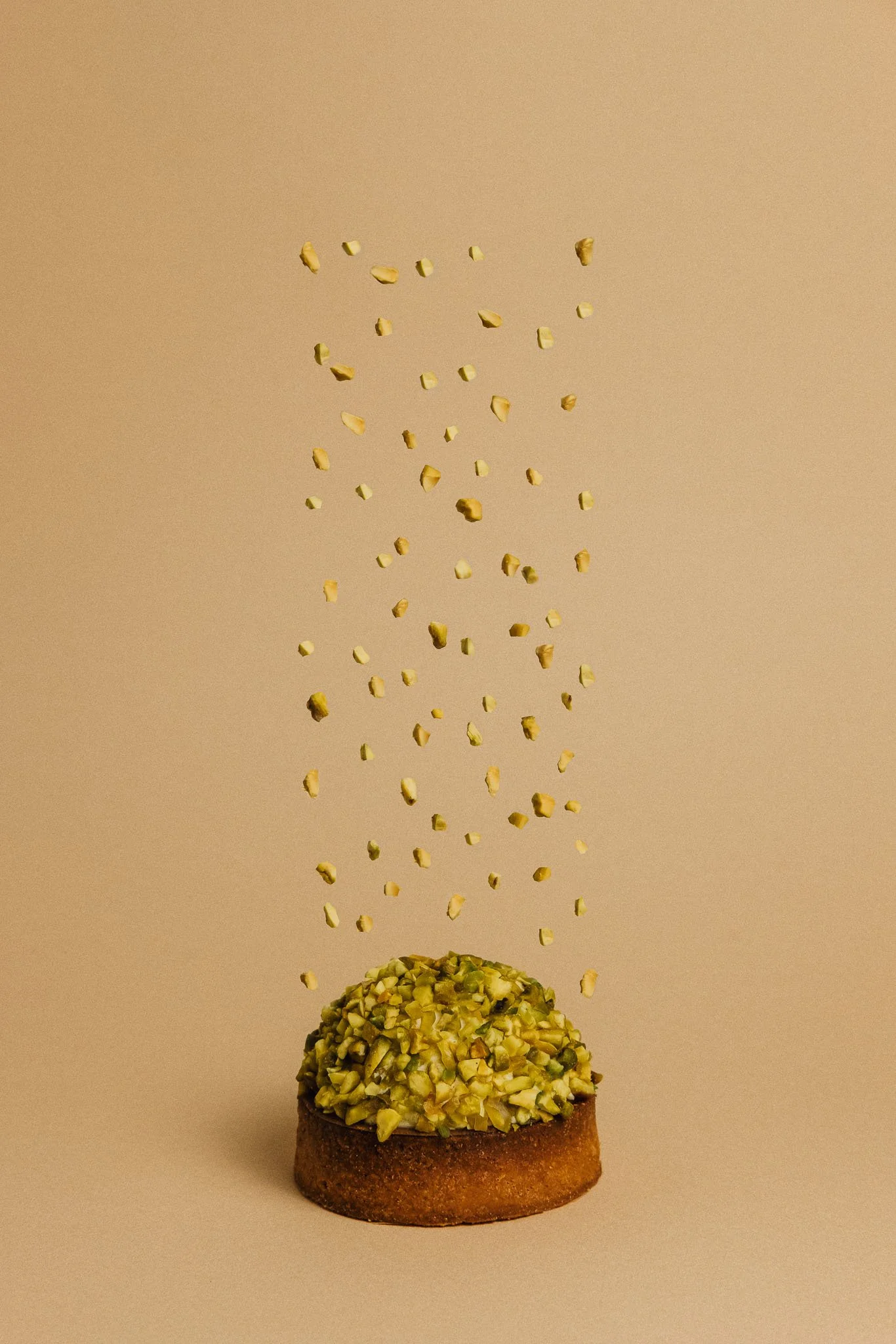 Un gâteau rond avec une surface recouverte de pistaches hachées, avec des morceaux de pistaches qui tombent du ciel.