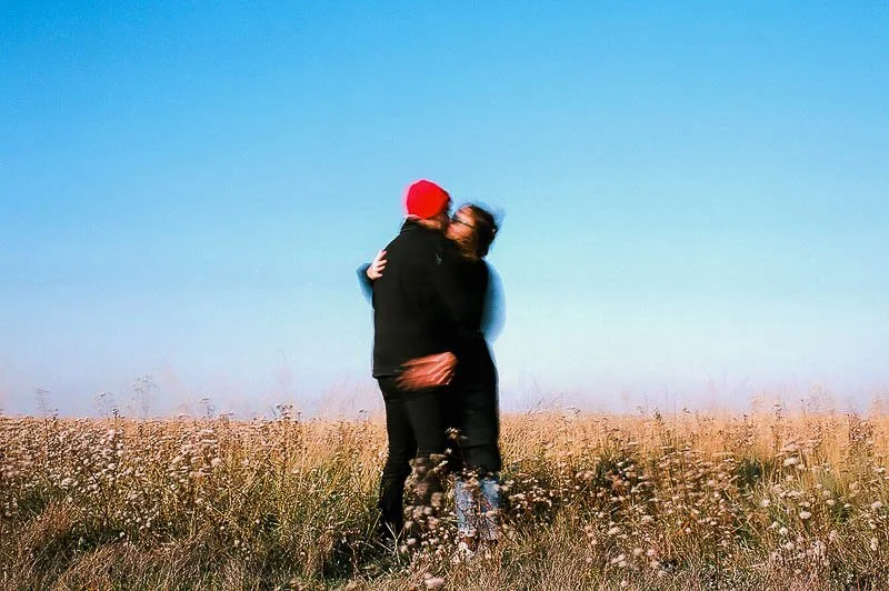 Deux personnes s'embrassent dans un champ d'herbes avec un ciel bleu clair en arrière-plan.