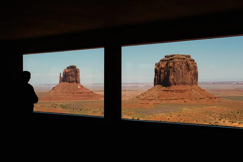 Silhouette d'une personne regardant par une fenêtre sur un paysage désertique avec deux formations rocheuses.