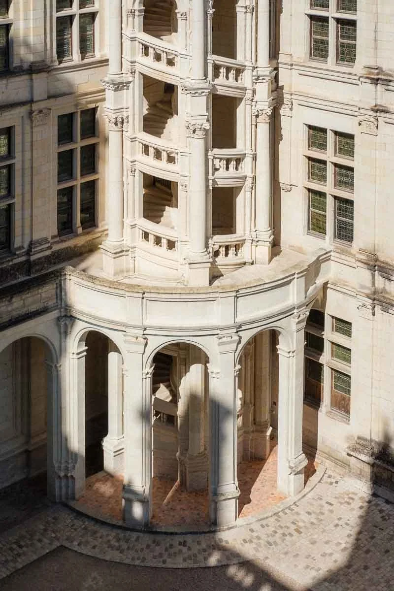 Vue d'un escalier en colimaçon blanc avec des balustrades dans un bâtiment historique en pierre.