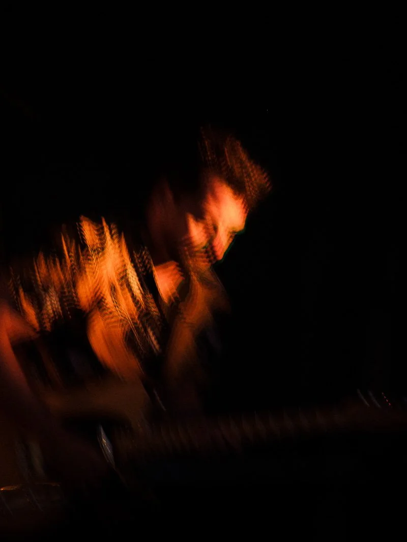 Portrait flou d'un guitariste sous un éclairage chaud dans l'obscurité.