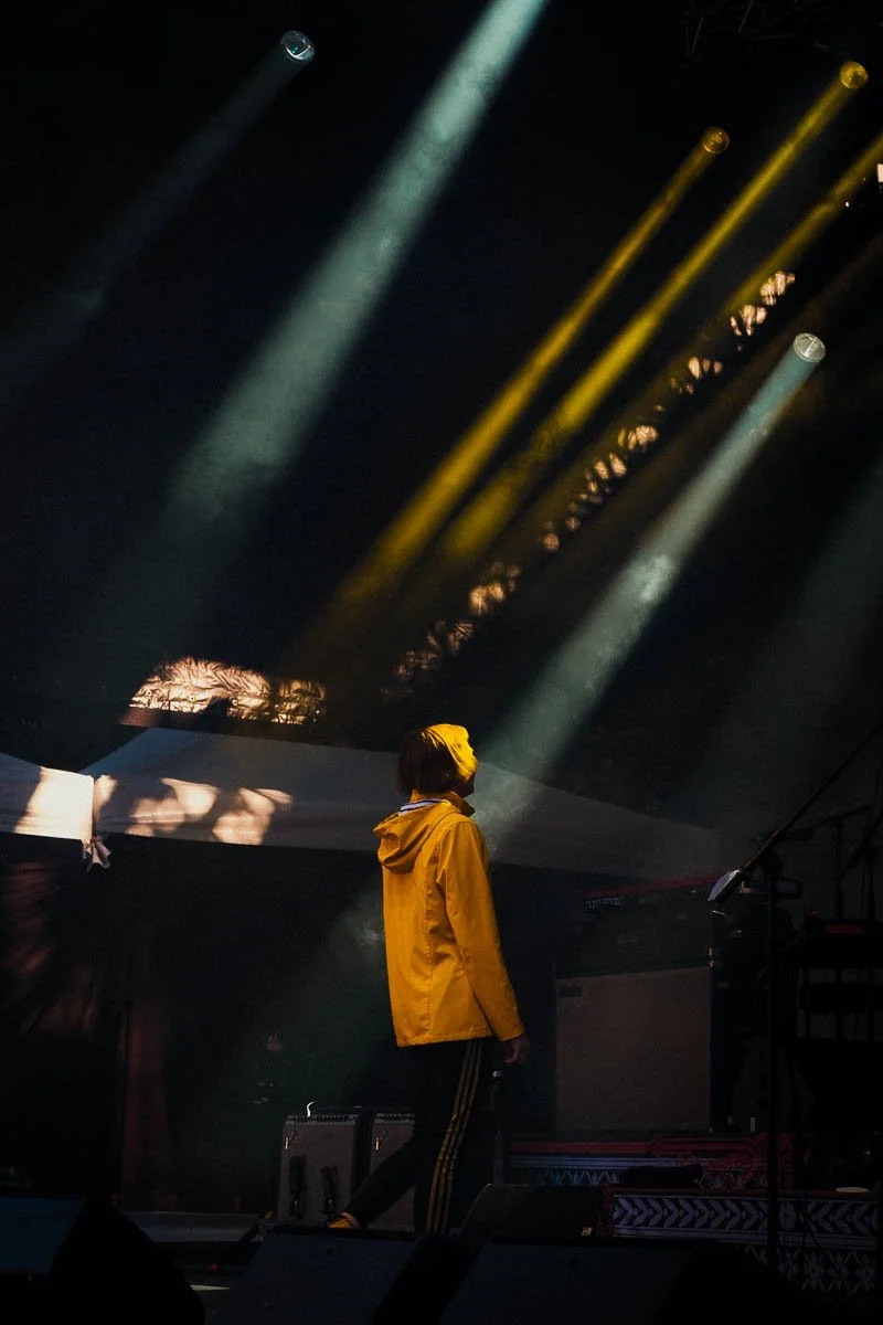 Chanteuse en veste jaune se tient sur une scène sombre avec des projecteurs de scène lumineux en arrière-plan.