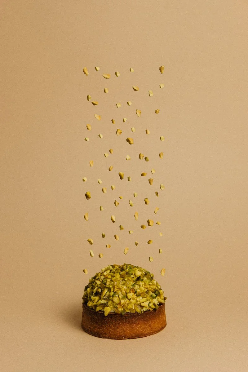 Un gâteau avec des pistaches en dessous, avec des morceaux de pistaches suspendus en l'air au-dessus.