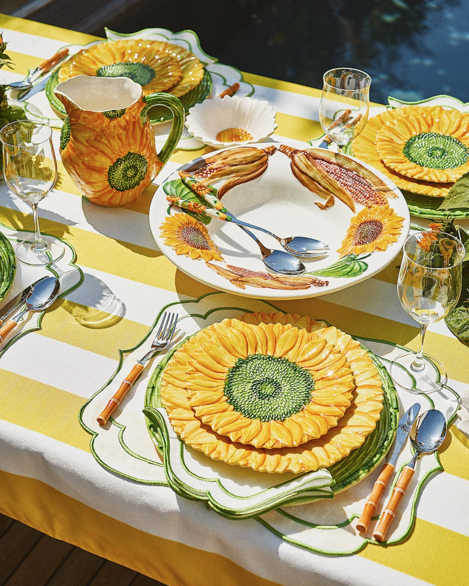 A table set for a meal with sunflower-themed dishes, cups, and utensils, featuring sunflower-shaped plates, a sunflower pitcher, and sunflower-themed plates and napkins.
