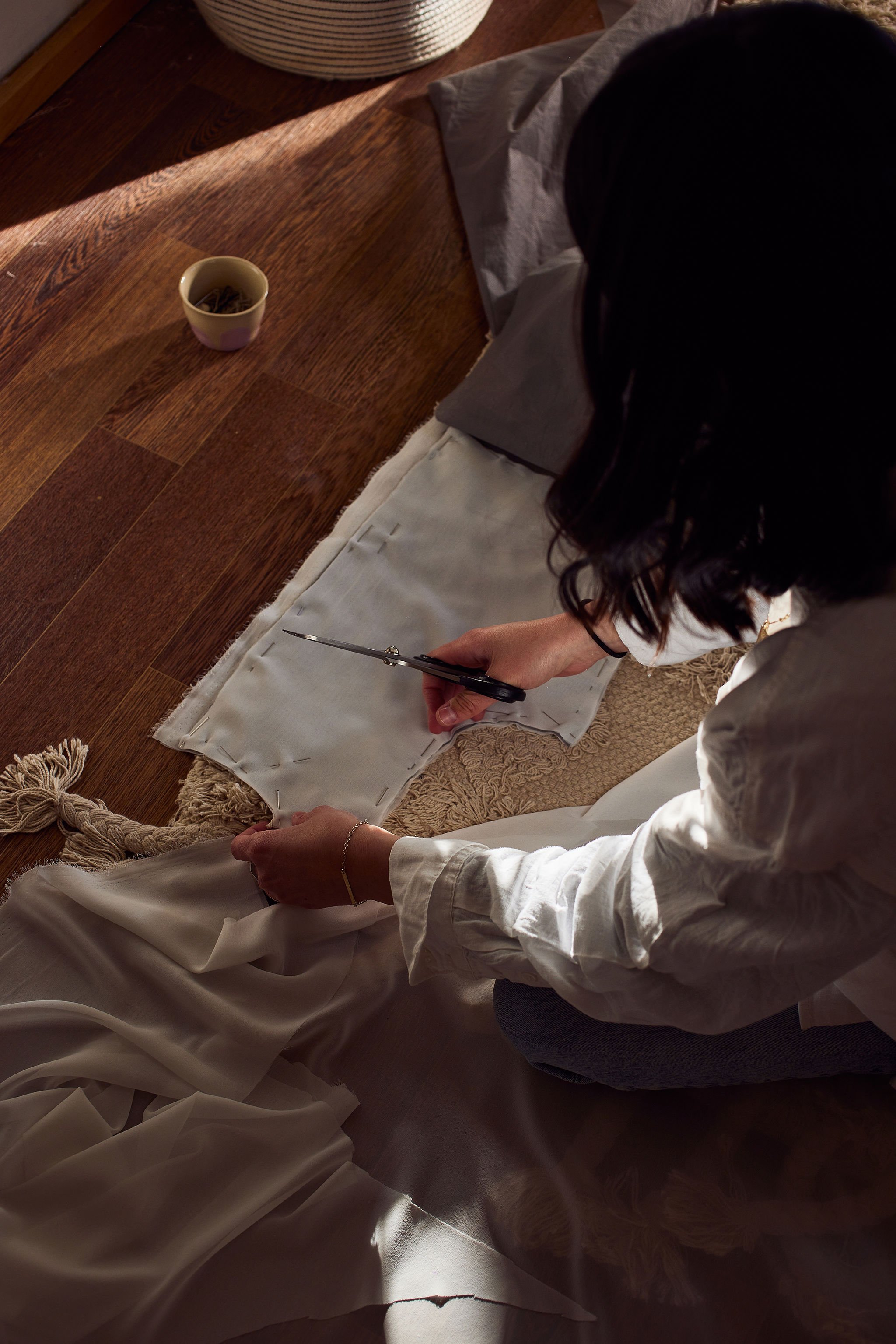 Person cutting fabric with scissors on the floor in a sunlit room.
