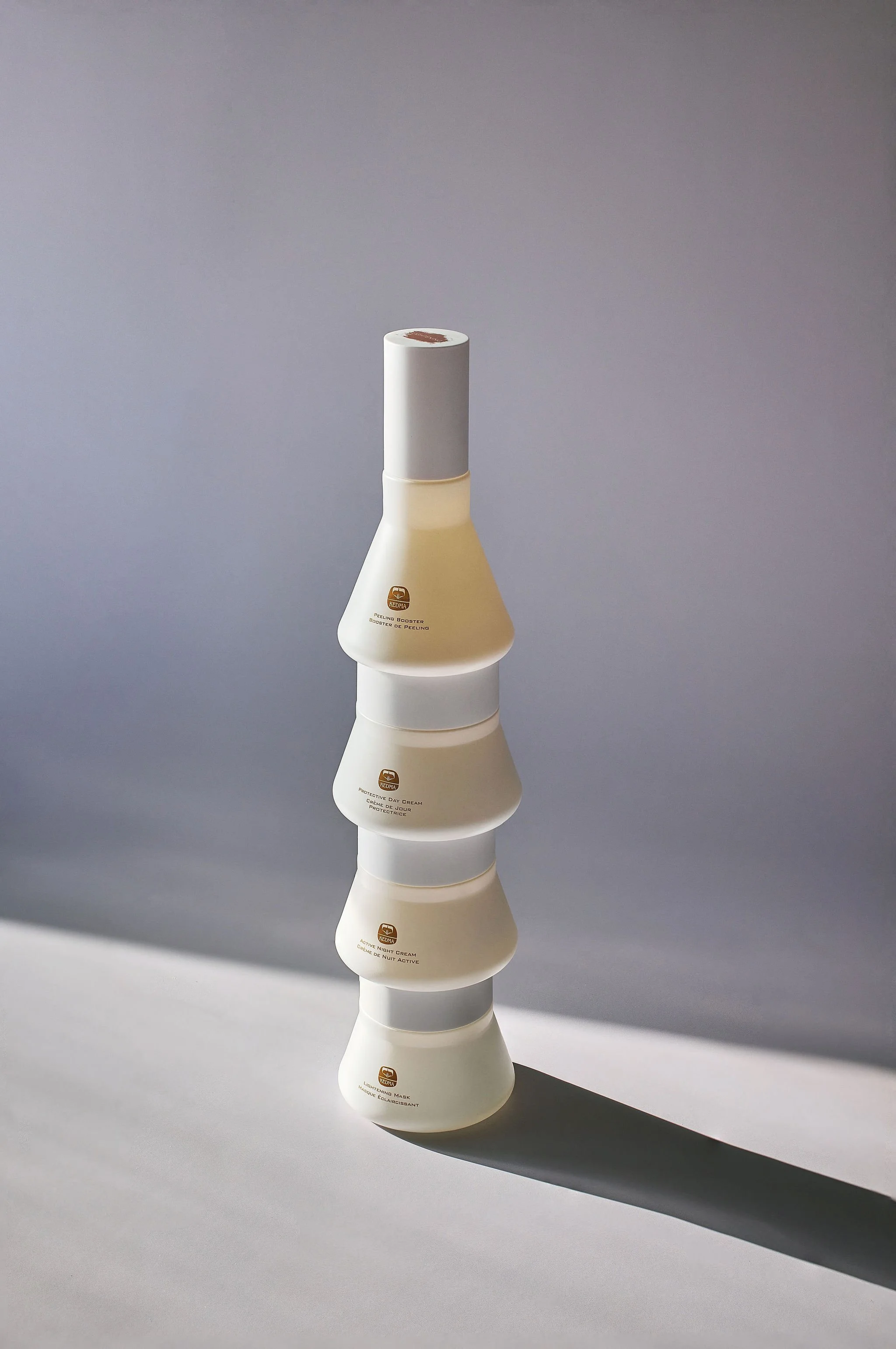 Stacked jars of skincare products on a light surface with a shadow, background is plain and light-colored.