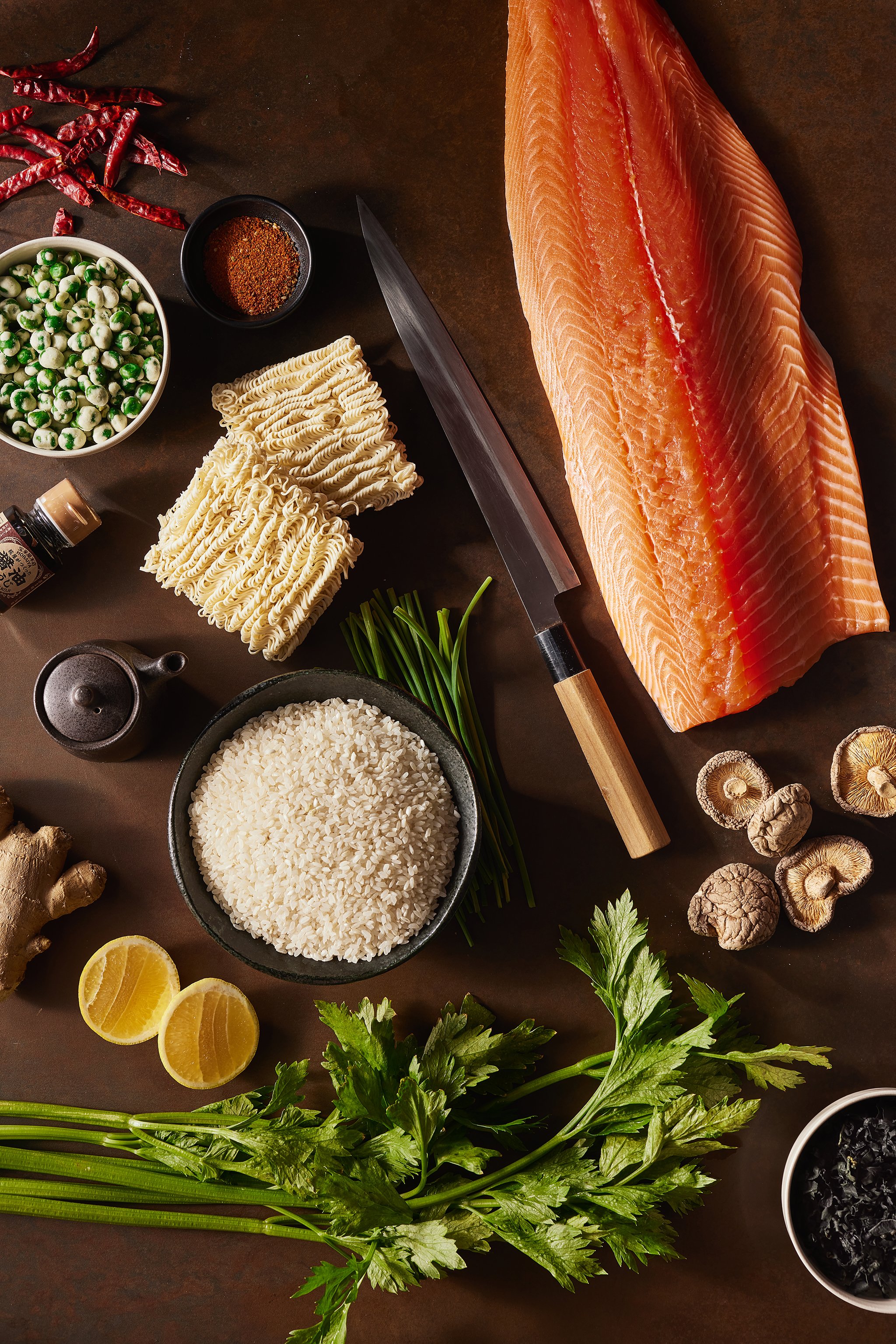 Fresh ingredients for cooking sushi, including a large salmon fillet, rice, dried mushrooms, green onions, lemon slices, ginger, seaweed, ramen noodles, dried red chili peppers, and various spices and herbs.