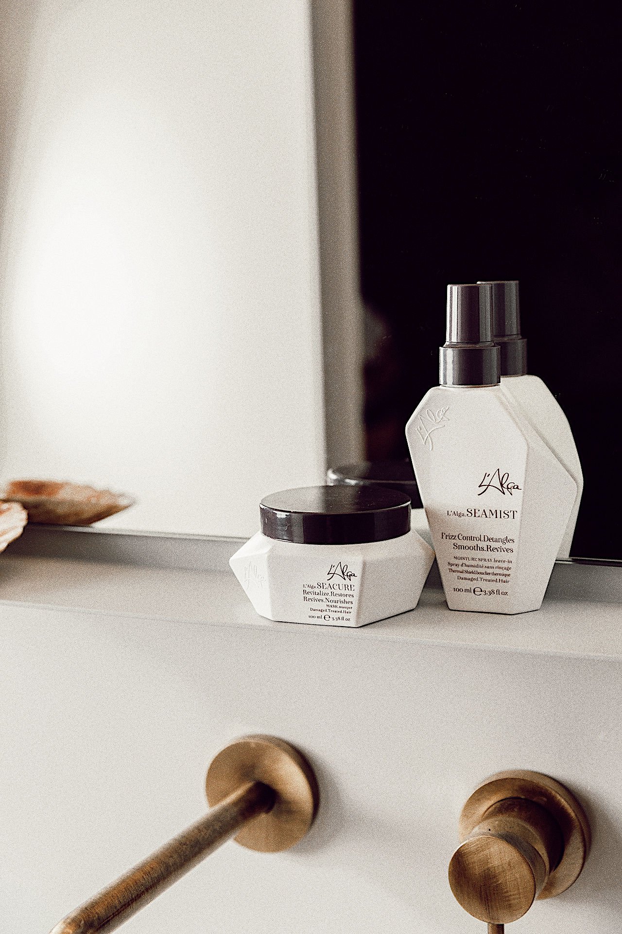 Beauty products on a white dresser, including a small jar and a spray bottle, with a mirror in the background and wooden drawer knobs.