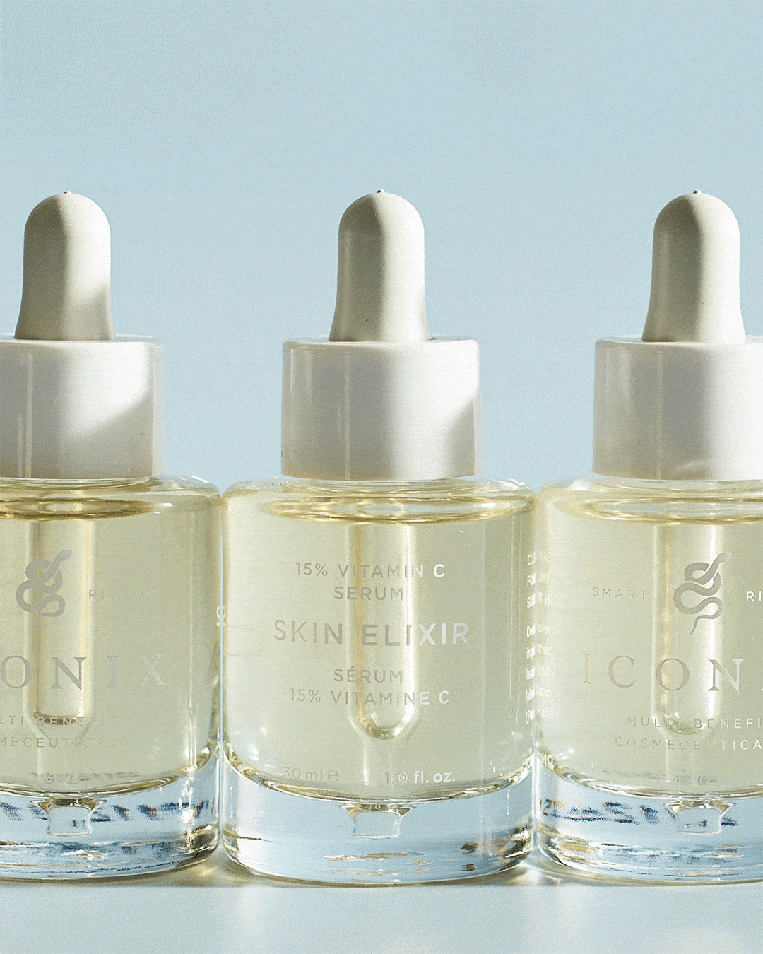 Three bottles of serum with white droppers labeled 'Skin Elixir' containing 15% Vitamin C, positioned against a light blue background.