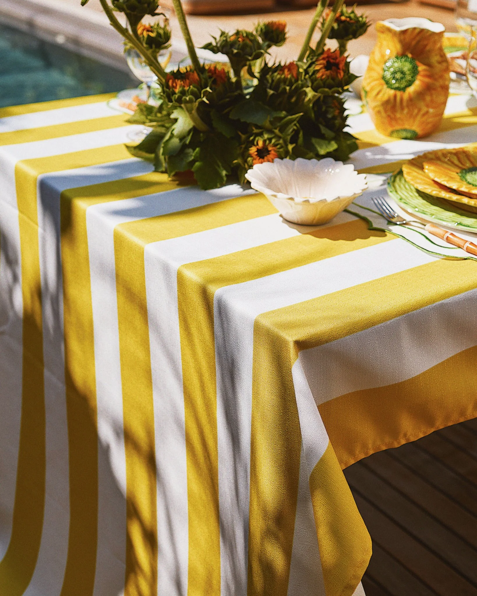 Table with yellow and white striped tablecloth, floral centerpiece, dishes, and utensils.