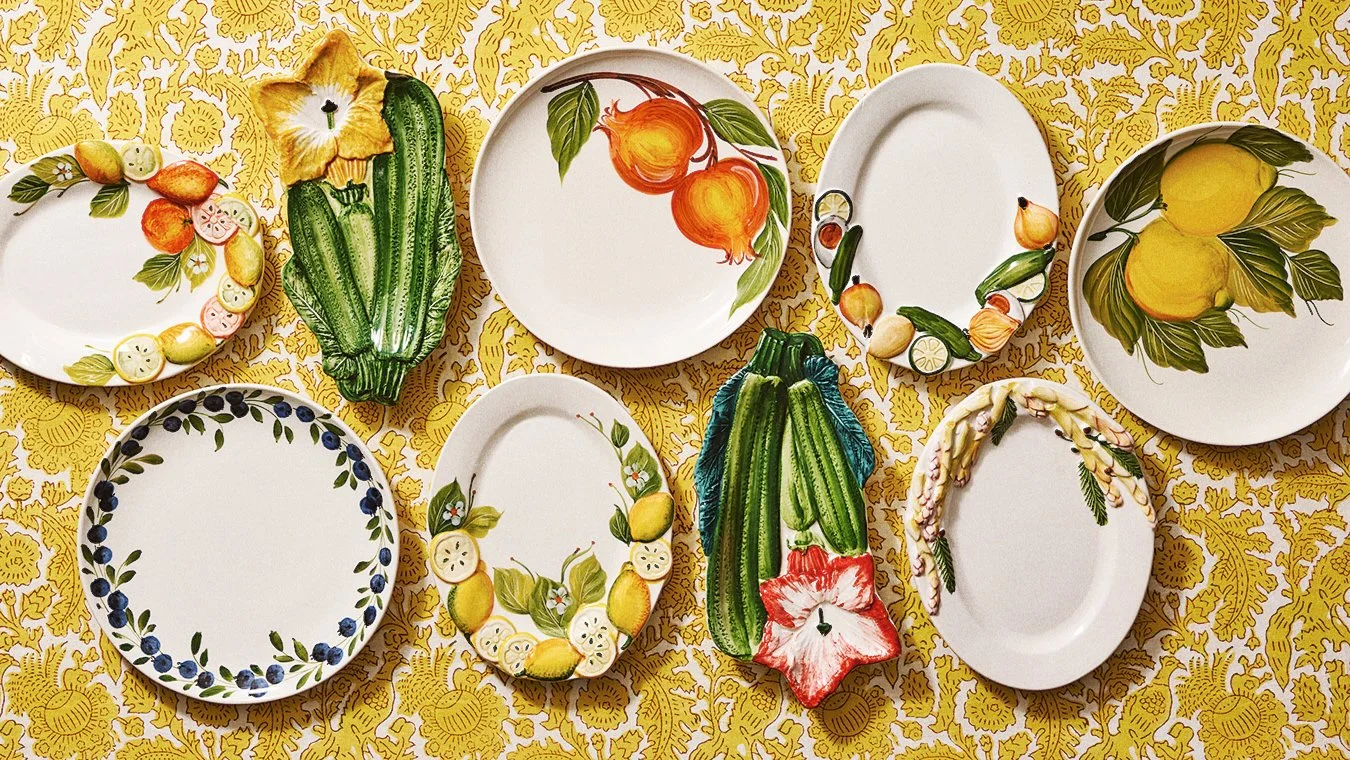 Decorative ceramic plates with fruit and vegetable patterns arranged on a yellow tablecloth.