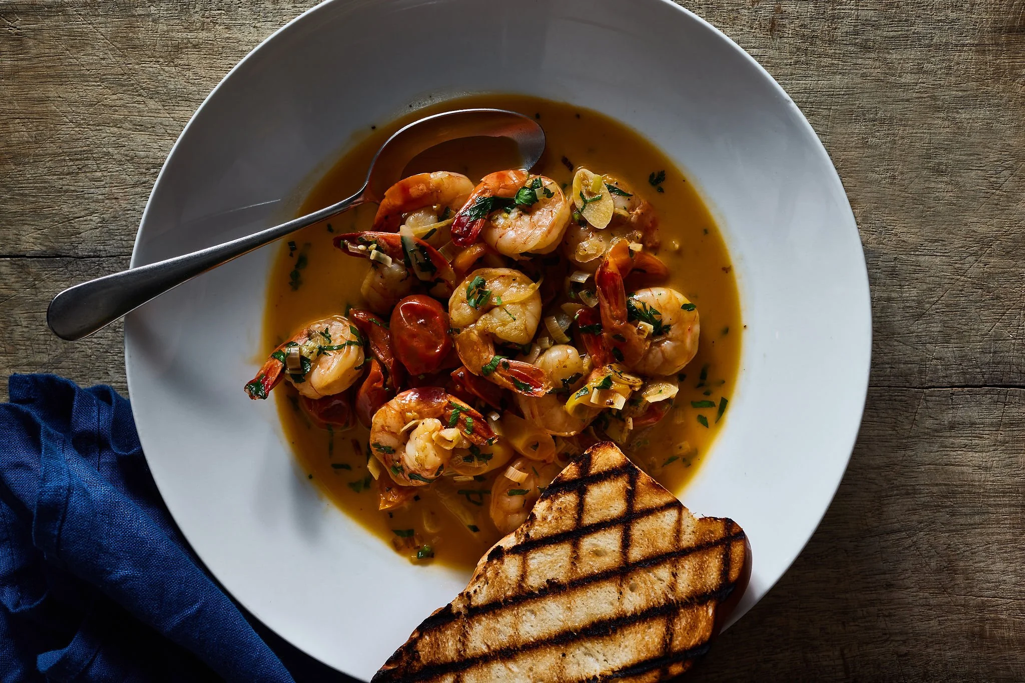 Shrimp and cherry tomato dish with a grilled sandwich on a white plate