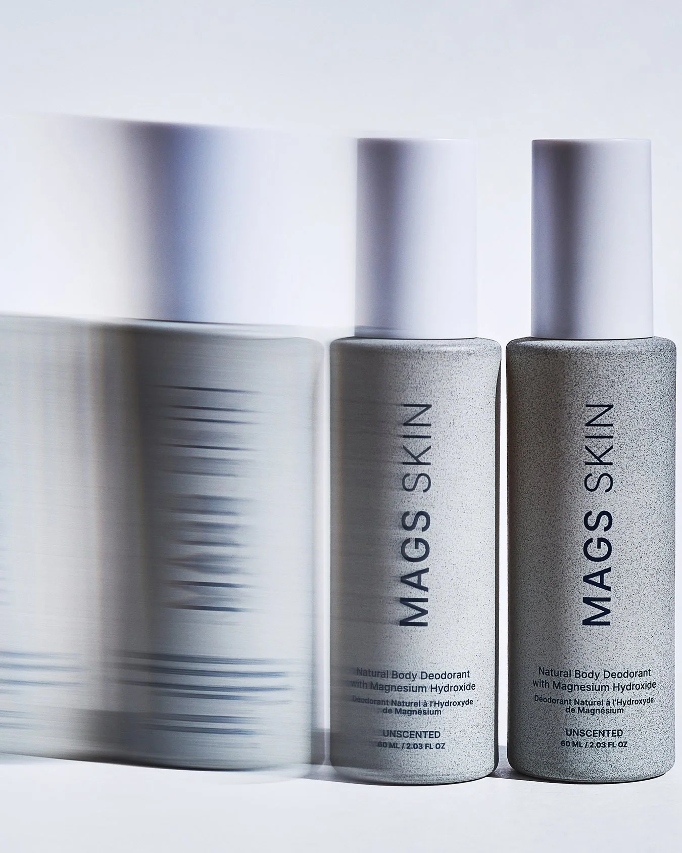 Two cans of MAGIC SKIN natural body deodorant with magnesium hydroxide, one in motion creating a blurred effect, and one stationary, both in a minimalist silver design.