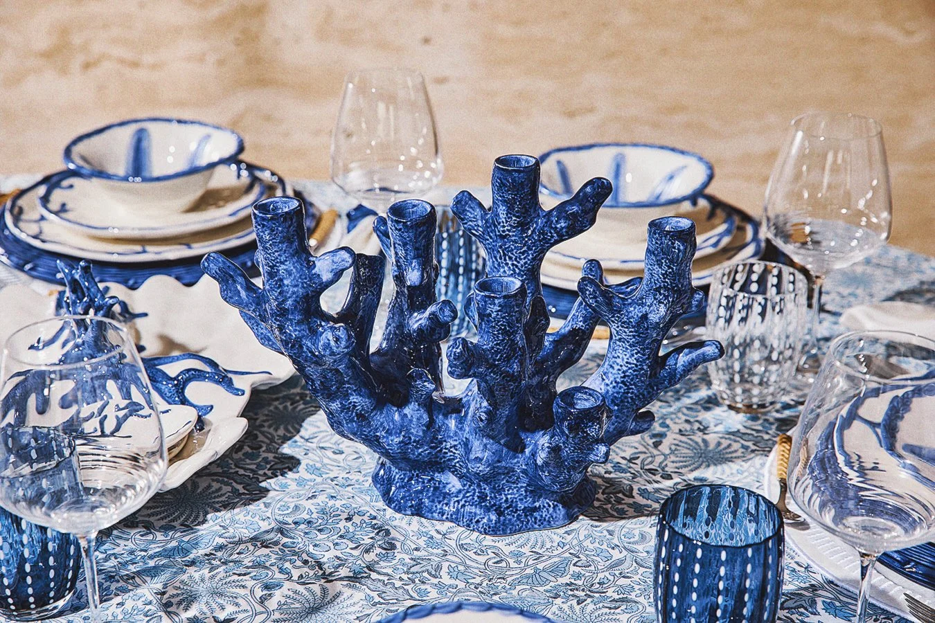 A table set with blue and white dinnerware, drinking glasses, and a large decorative blue coral centerpiece.