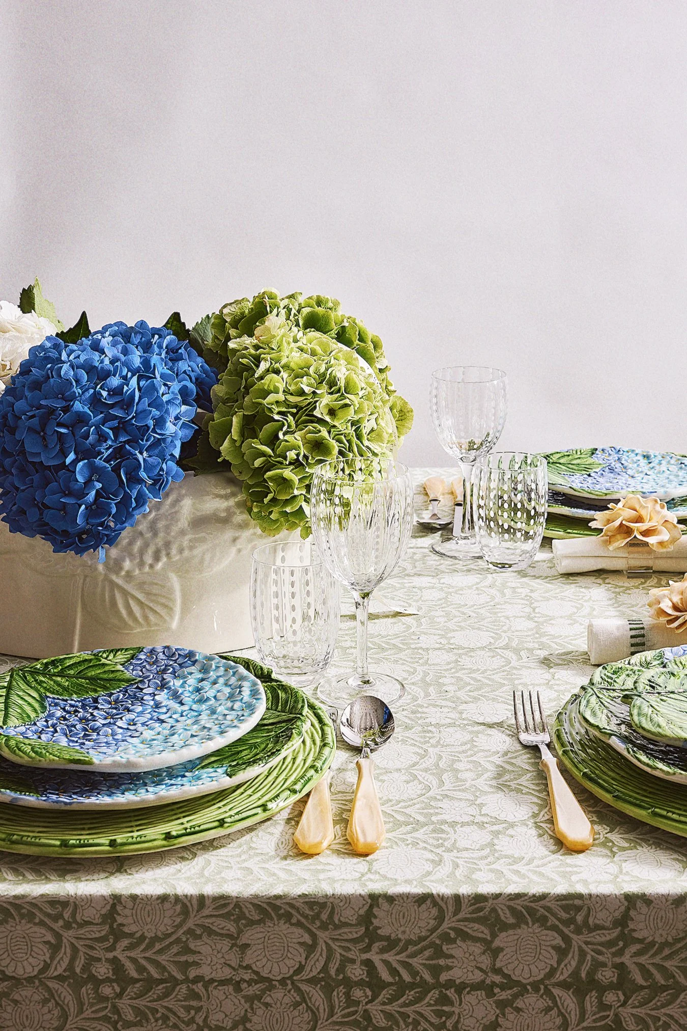 Elegant dining table with floral-themed plates, glasses, and cutlery, decorated with a large bouquet of blue and green hydrangeas.