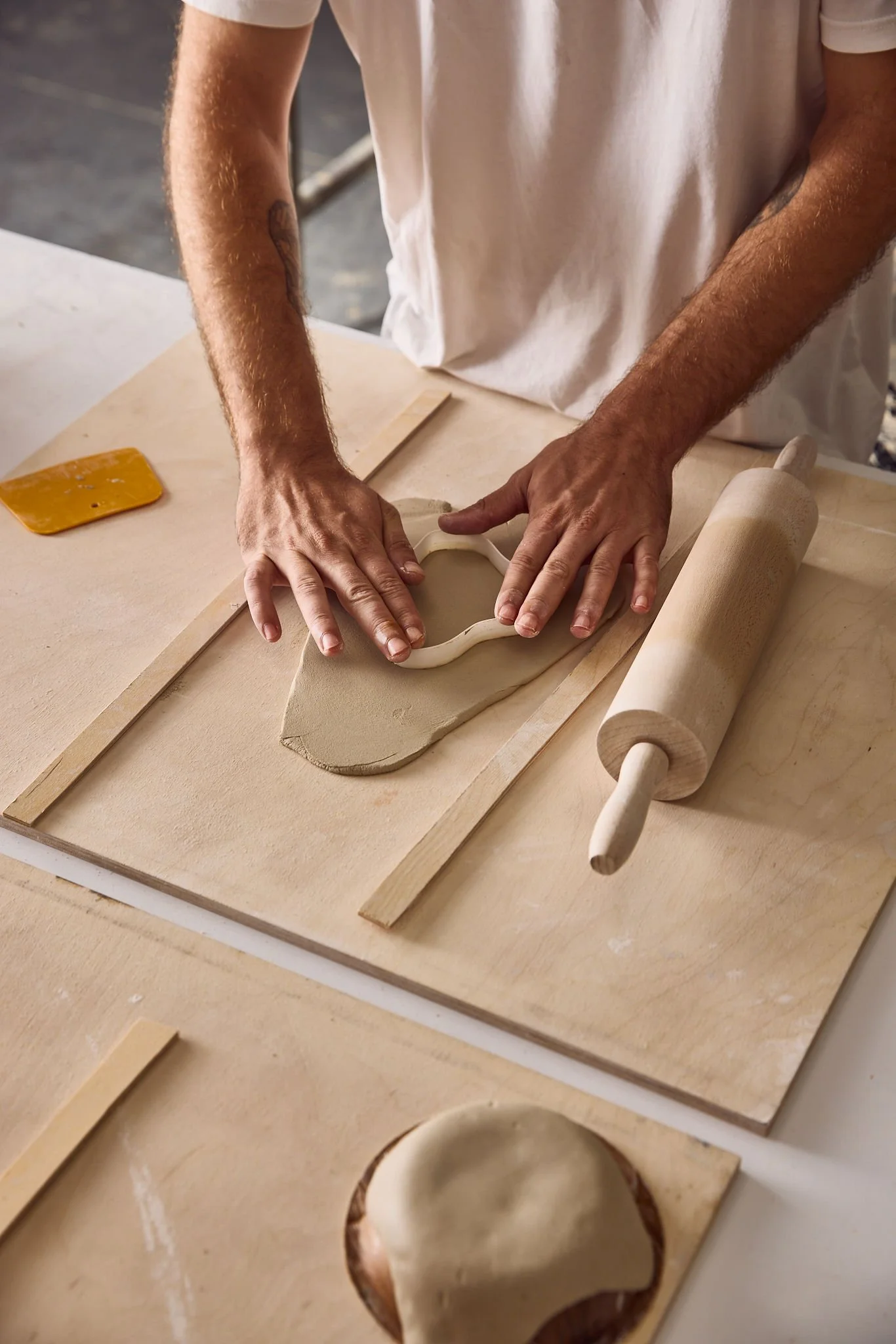 Person rolling out clay with a rolling pin and cutting shapes with a cookie cutter in a pottery studio.