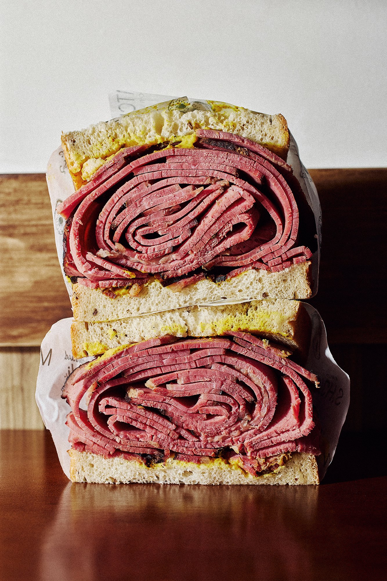 Two stacked Italian cold cut sandwiches with thin slices of ham, roast beef, and bread, served on a wooden surface.