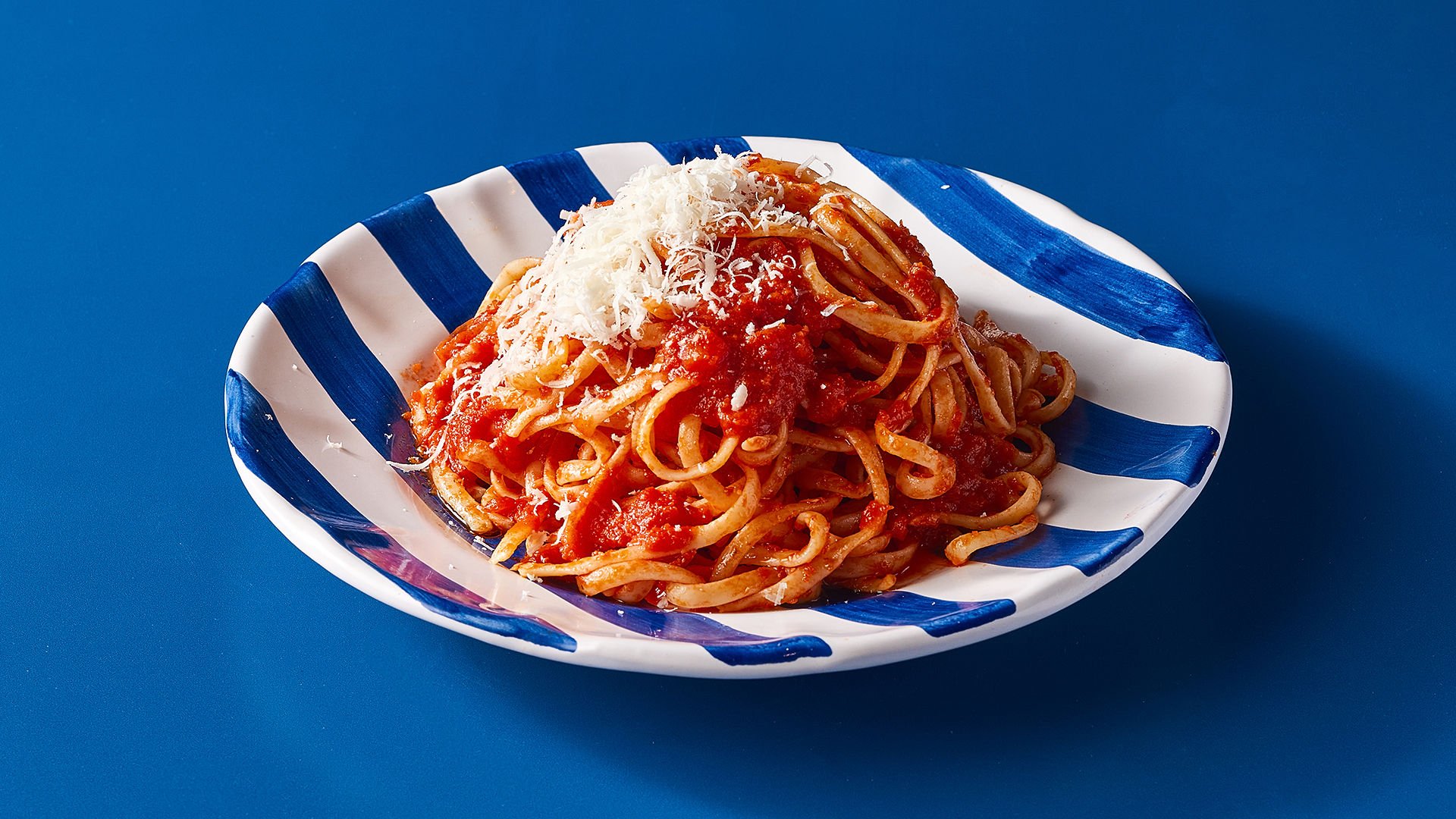 Plate of spaghetti with tomato sauce and grated cheese on top, served on a blue and white striped dish with a blue background.