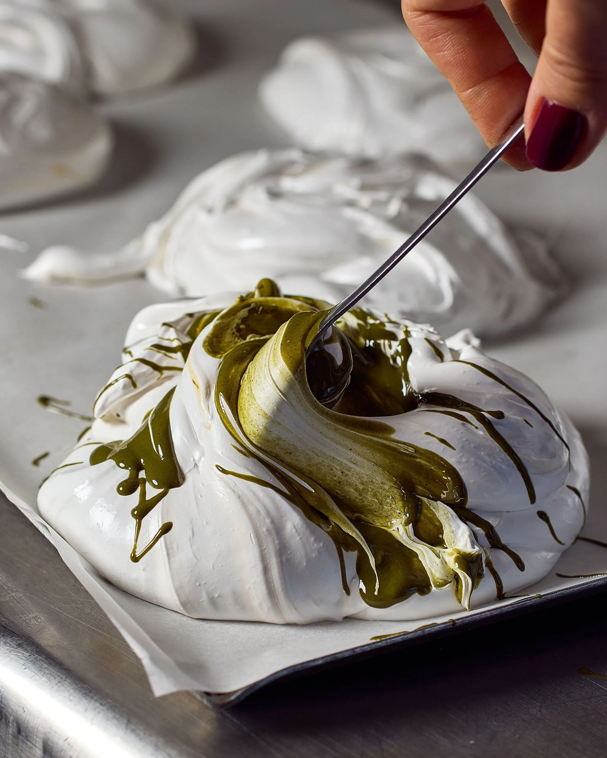 Close-up of a toasted meringue dessert with chocolate and matcha drizzle, with a person inserting a fork into it.