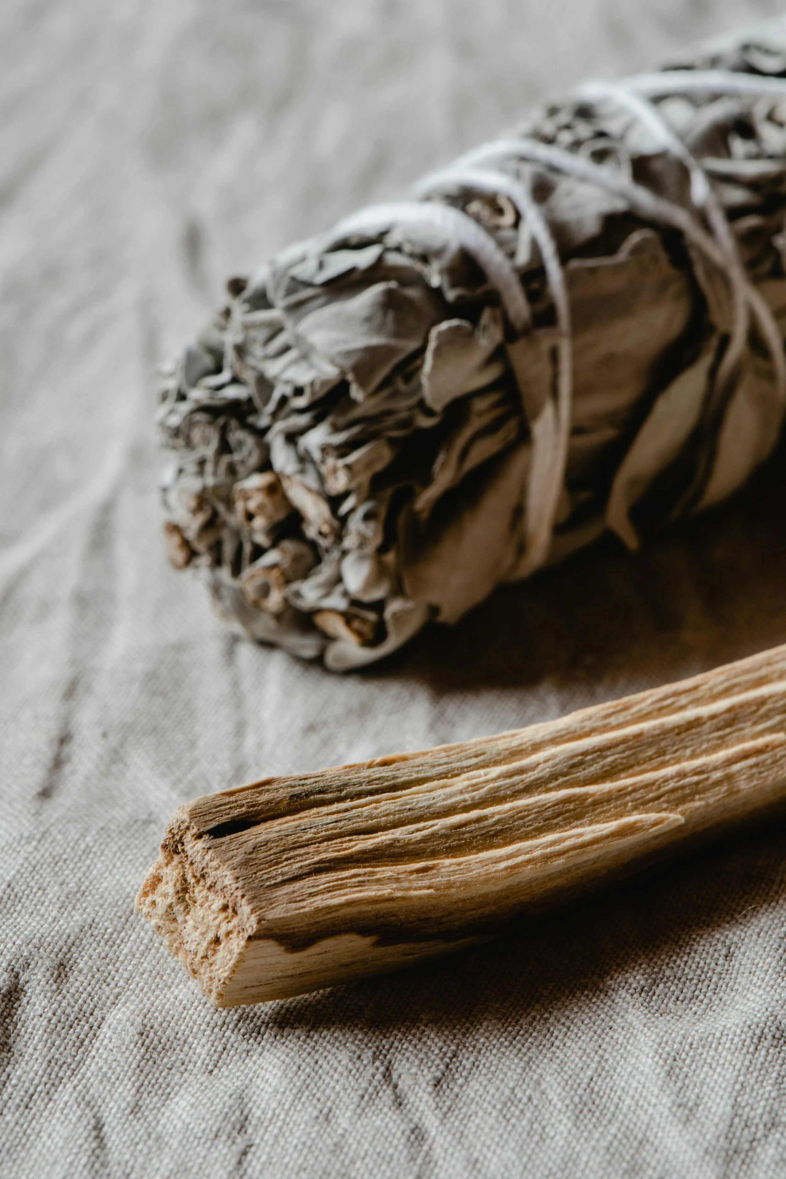 A bundle of dried sage tied with string and a palo santo stick resting on a cloth surface.