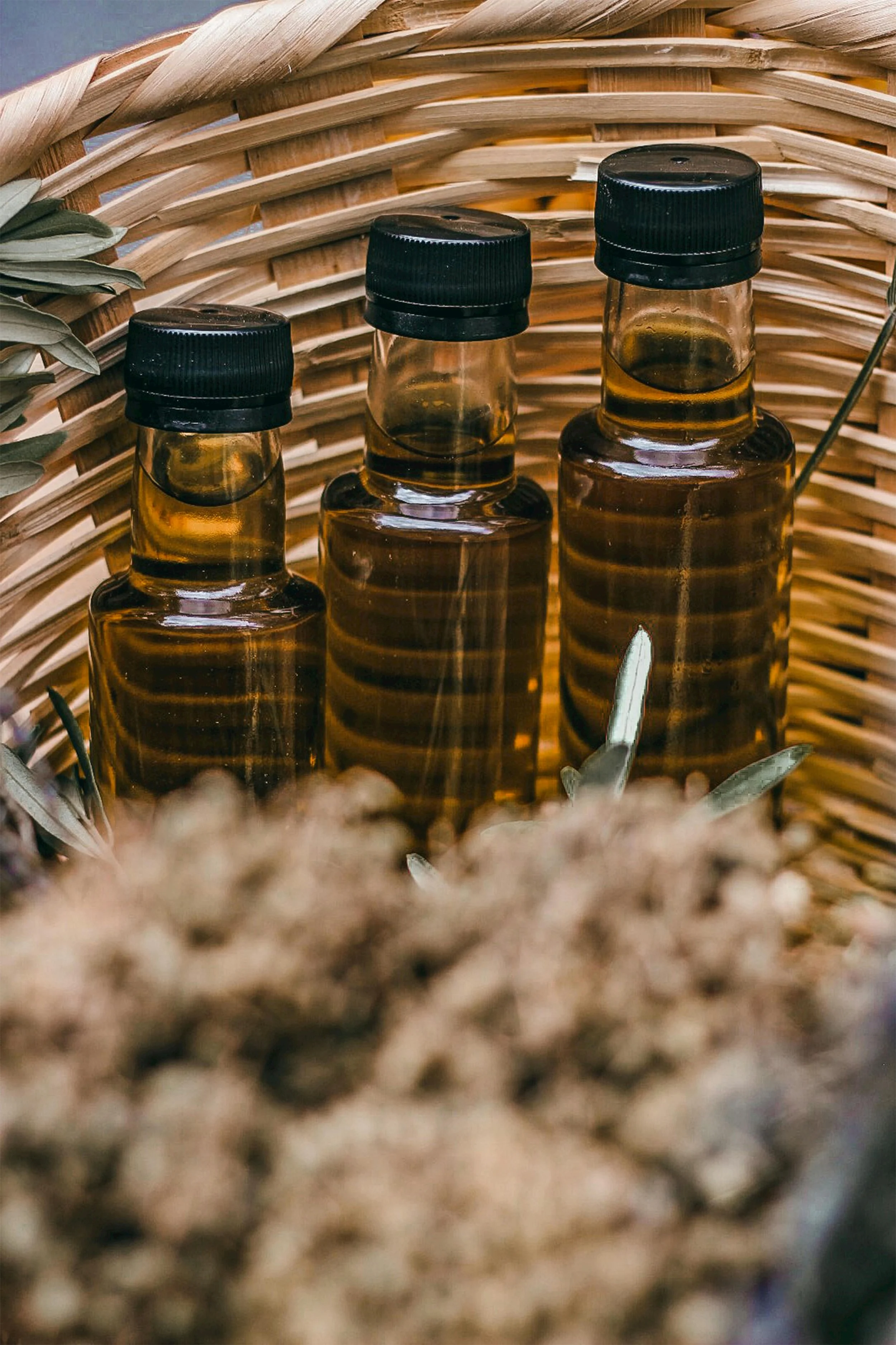 Three small amber glass bottles with black caps inside a woven basket with dried plants around them.