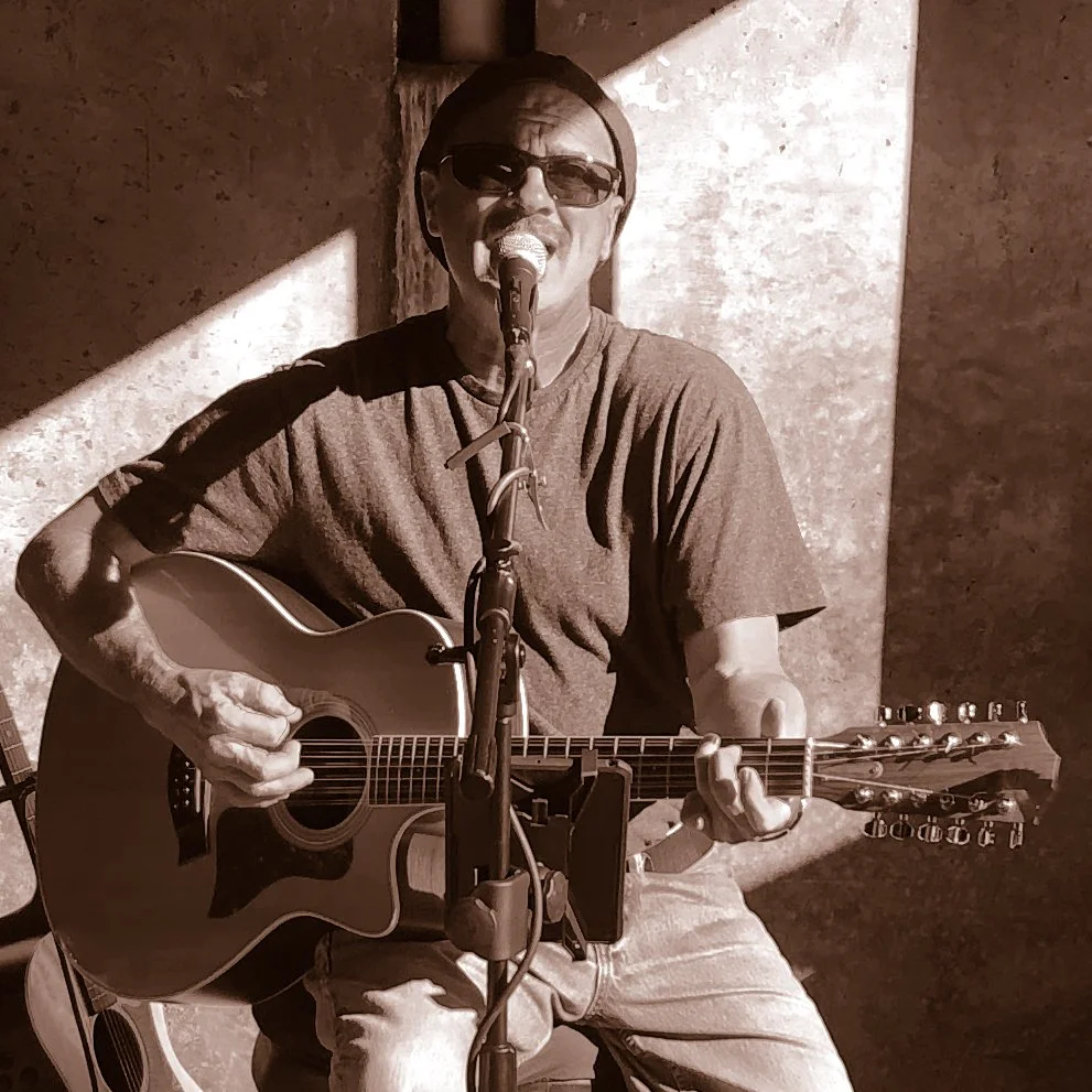 Eric Zobel seated with a guitar singing into a mic. The photo is a sepia tone