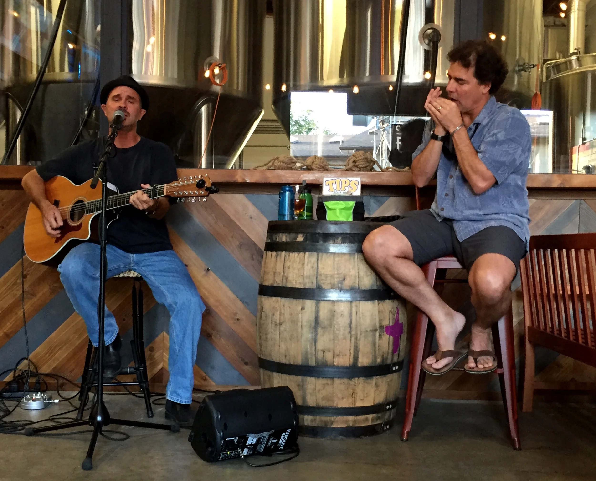Eric Zobel seated with a guitar singing in a brewery with another musician playing harmonica
