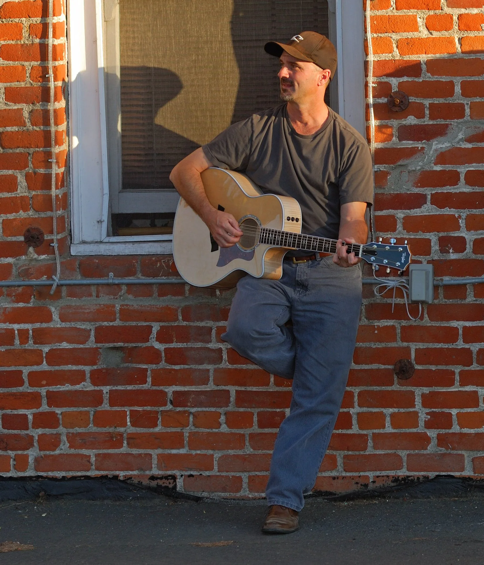 Eric Zobel standing with a guitar in front of a brick wall