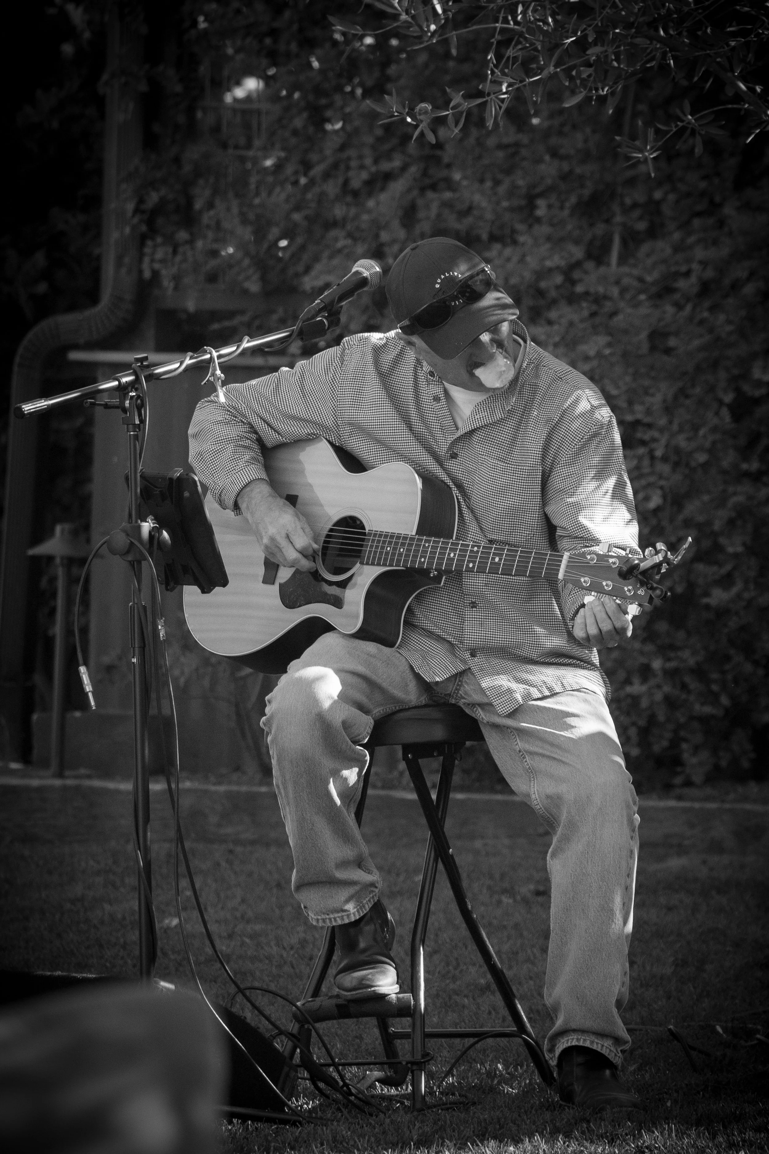 Eric Zobel seated with a guitar singing into a mic the photo is black and white