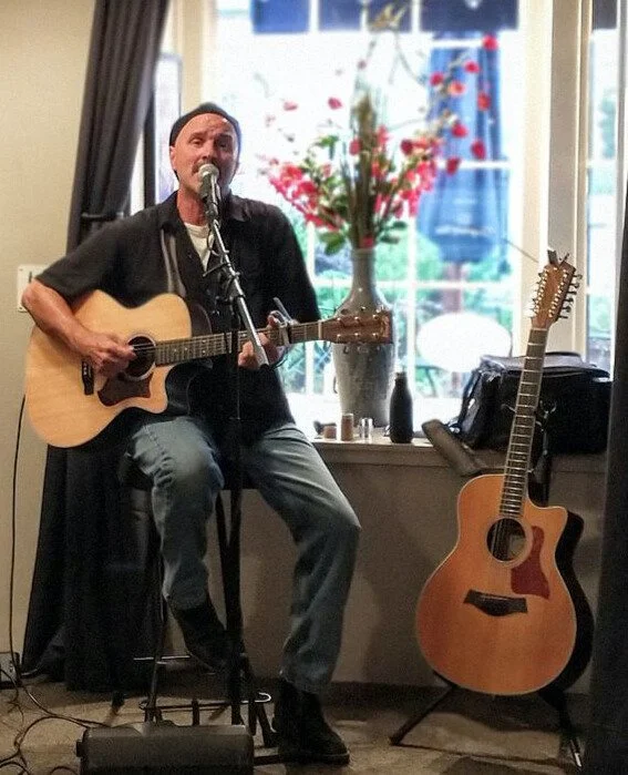 Eric Zobel seated with a guitar singing into a mic